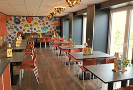 Modernes�Restaurant�der Jugendherberge Idar-Oberstein mit orangefarbenen St�hlen und einer kreativen Wandgestaltung aus bunten, kreisf�rmigen Edelstein-Motiven.