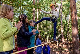 Ein Mädchen balanciert auf einem Seil. Die Schulklasse jubelt.
