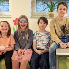 Zwei Mädchen und zwei Jungen sitzen nebeneinander und lachen in die Kamera