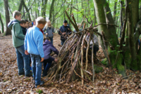 Survival light im Wald: Schüler arbeiten zusammen an einem Unterschlupf aus Naturmaterialien während eines Klassenfahrt-Programms.